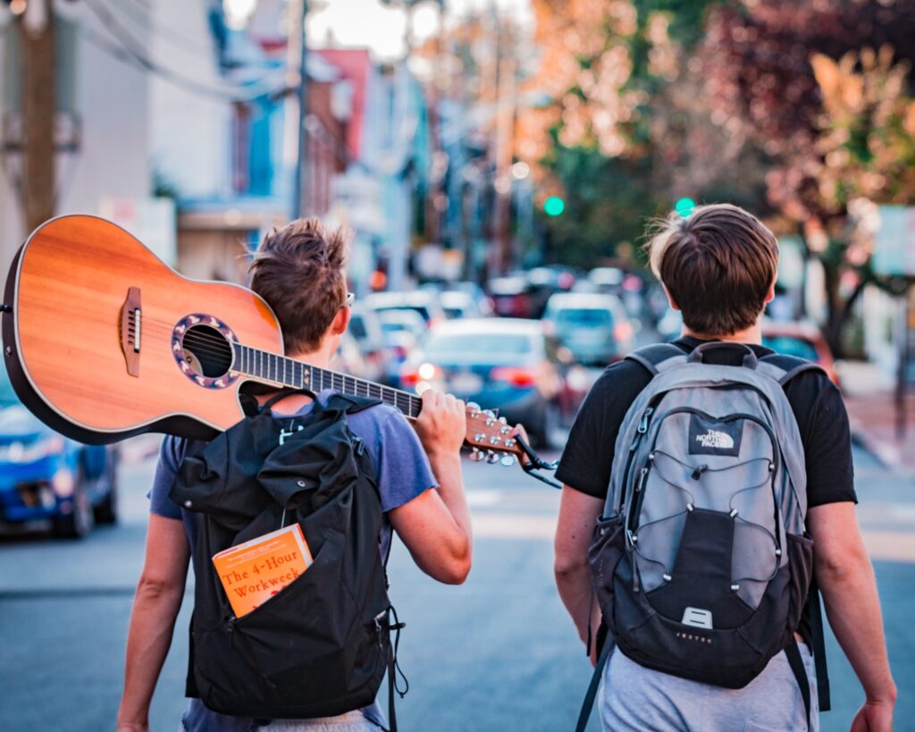 Two travelers, one with a book and guitar, walking through a city, by Austin Distel from Unsplash